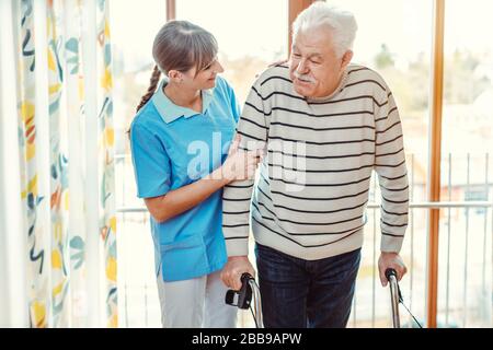 Infirmière aidant l'homme principal avec cadre de marche dans la maison de soins infirmiers Banque D'Images