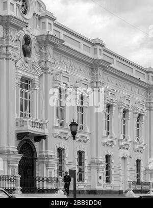 OTAVALO, ÉQUATEUR - 28 JUILLET 2018 : une photo en noir et blanc d'un homme en costume marchant devant la municipalité GAD d'Otavalo. Banque D'Images