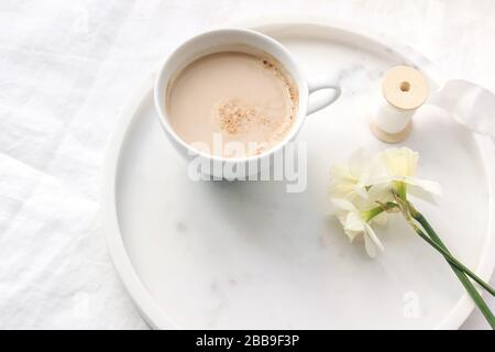 Mariage de printemps toujours la composition de la vie. Gros plan de la tasse de café avec du lait, du ruban de soie, des narcisses, des fleurs de daffodil sur plateau de marbre Table de linge blanc c Banque D'Images