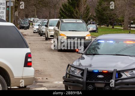 Detroit, Michigan, États-Unis. 30 mars 2020. Les gens ont attendu dans leur voiture dans un site de distribution de Gleaners Food Bank dans un quartier très hispanique. Le besoin de nourriture a augmenté de façon spectaculaire à Detroit la semaine dernière. Sur ce site, la nourriture a manqué alors que beaucoup attendaient encore, et un policier a fait descendre la ligne de voitures en transmettant le message sur son haut-parleur: "Pas de mas comida" (plus de nourriture). Crédit: Jim West/Alay Live News Banque D'Images