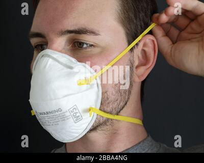 On montre qu'un homme pose un masque de protection contre le crépuscule blanc N95 de manière rapprochée, placé sur un fond sombre. Banque D'Images