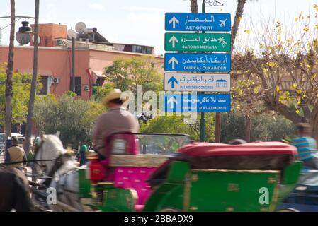 Un signe directionnel à Marrakech, écrit en arabe et en français. Entouré de moyens de transport dans le flou de mouvement, suggérant la vitesse. Banque D'Images