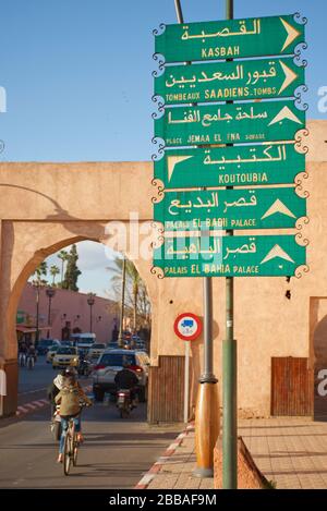 Un signe directionnel à Marrakech, écrit en arabe et en français. Entouré de moyens de transport dans le flou de mouvement, suggérant la vitesse. Banque D'Images
