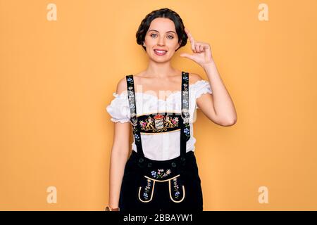 Jeune belle femme allemande aux yeux bleus portant une robe traditionnelle d'octoberfest souriant et confiant gestuelle avec la main faisant un petit signe de taille avec Banque D'Images