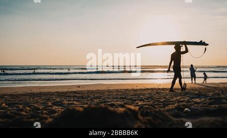 Les silhouettes des surfeurs marchent sur la plage au coucher du soleil Banque D'Images