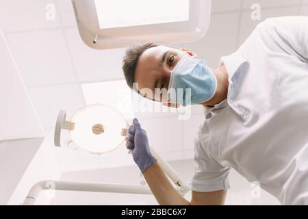 Un médecin dentaire professionnel travaille au bureau. Le dentiste tient une lampe dentaire pour examiner le patient. Le concept d'un rendez-vous avec un médecin dans une clinique. Banque D'Images