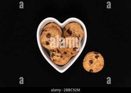 Cookies aux pépites de chocolat dans un bol en forme de coeur sur fond noir. Banque D'Images