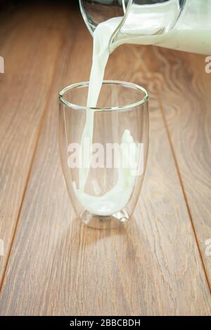 Prenez le lait d'un pichet dans un verre sur une table en bois éclabousse de lait. Banque D'Images