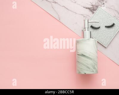Flacon de shampooing ou de pompe à gel et fausses cils isolés deux couleurs de marbre de couleur et un fond rose. Image horizontale de la vue de dessus et de la couche plate Banque D'Images