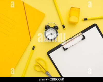 Fournitures de papeterie pour l'école, concept de retour à l'école. Presse-papiers en papier, ciseaux jaunes, réveil noir, ordinateur portable, crayons et isolat d'aiguiseur jaune Banque D'Images
