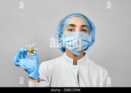 Médecin féminin en uniforme médical de protection tenant le coronavirus. Virologue scientifique tenant dans les mains le modèle artisanal de nouveau Coronavirus ou COVID-19 Banque D'Images