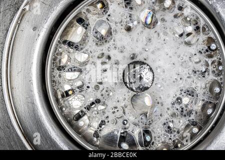 Mousse blanche avec bulles de nettoyant dans un lavabo, vue macro. Vidanger le trou avec des bulles de savon dans l'évier métallique. Bouchon de vidange réglable mécaniquement. Banque D'Images