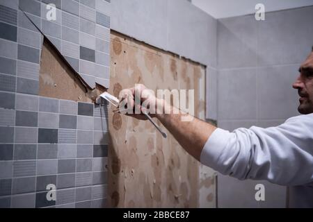 le travailleur professionnel enlève démolir les vieux tuiles dans une salle de bains avec marteau et burin Banque D'Images