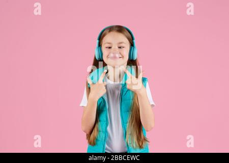 Une petite fille avec casque explose la gomme à mâcher rose sur un fond rose. Banque D'Images