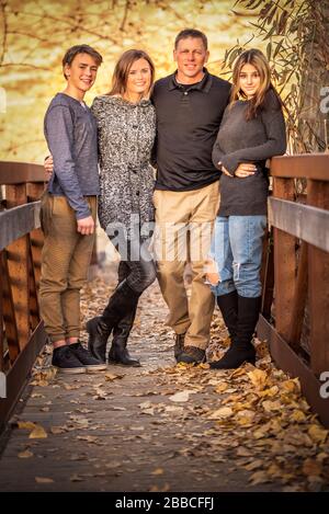 Portrait des parents et de leurs adolescents souriant, debout et embrassant sur le pont pendant l'heure d'or. Banque D'Images