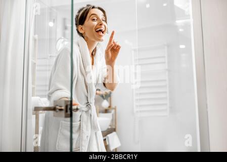 Jeune et joyeuse femme en peignoir allant à la salle de bain, fermant une porte en verre à la maison Banque D'Images