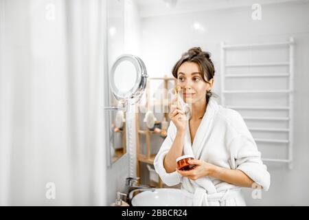 Jeune femme massant le visage pendant les procédures d'hygiène dans la salle de bains Banque D'Images