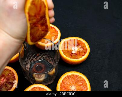 une main presse le jus de la moitié de l'orange rouge dans une tasse en verre. Jus frais Banque D'Images