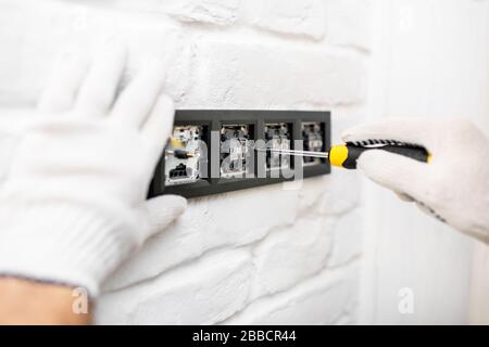 Électricien installant des prises et des interrupteurs sur le mur de briques blanches, gros plan Banque D'Images
