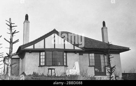 Circa 1930s, une vue arrière d'un bungalow de l'époque, avec un lit de bébé décoré de dentelle et d'abat-jour assis sur le petit patio extérieur, Angleterre, Royaume-Uni. On pense que les premiers bungalows britanniques modernes ont été conçus par un architecte anglais, John Taylor et construits à Westgate-on-Sea, Kent en 1869 et 1870. Le mot bungalow est originaire de la région bengali de l'Inde, signifiant «maison dans le style Bengale. Banque D'Images