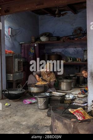 Un homme indien qui s'est couté sur le sol d'une petite cuisine crammée surmontée de pots Banque D'Images