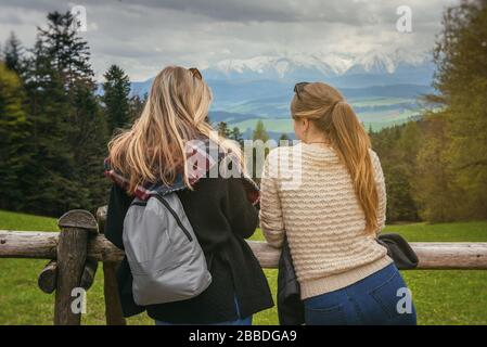 Photo de l'arrière de deux jeunes femmes près de la clôture en bois sur un paysage de montagne pittoresque, Pologne, Tatra Banque D'Images