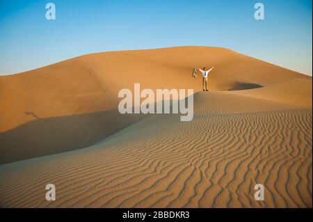 Homme d'affaires éloigné debout avec des armes soulevées sur la crête d'une grande dune de sable du désert Banque D'Images