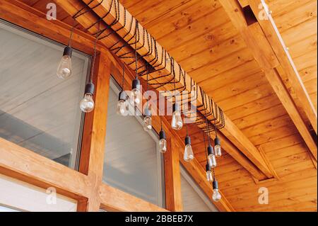 lampe de rue inhabituelle pour l'éclairage extérieur de la maison, les lampes sur les fils sont enroulées sur une poutre en bois à l'entrée d'une maison en bois élégante Banque D'Images