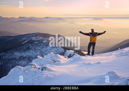 homme aux bras ouverts au-dessus de merveilleux paysage de montagnes dans la brume pendant la soirée d'hiver calme Banque D'Images