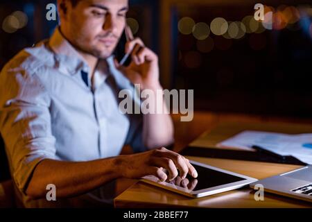 Homme d'affaires sérieux utilisant un ordinateur tablette assis au bureau la nuit Banque D'Images