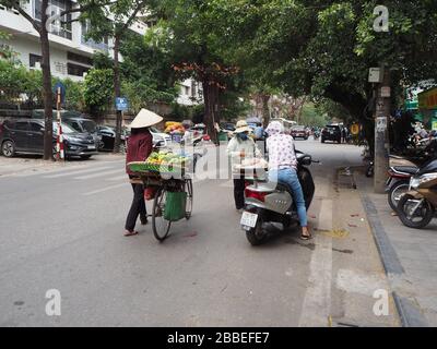 Les femmes sur les vélos qui vendent des fruits frais et d'autres aliments portent des chapeaux coniques et des masques pour la protection pendant la pandémie de coronavirus, Hanoi, Vietnam Banque D'Images