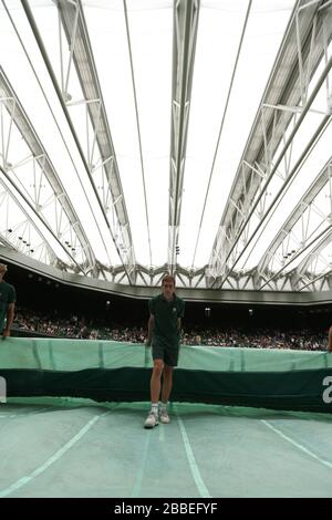 La course du personnel de terrain pour mettre les housses sur le court central pendant que les arrêts de pluie jouent pendant le match entre la Pologne Agnieszka Radwanska et la France Mathilde Johansson au cours du quatrième jour des championnats de Wimbledon au All England Lawn tennis and Croquet Club, Wimbledon. Banque D'Images