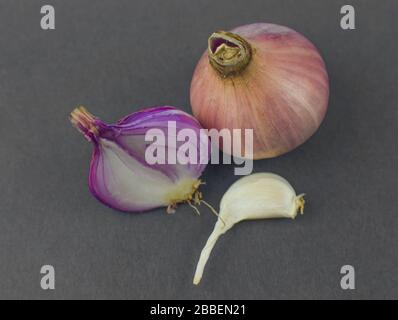 Un oignon de couleur rose demi-pelé placé à côté d'un oignon de taille moyenne non pelé et un morceau d'ail avant un fond noir Banque D'Images