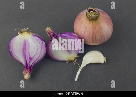 Deux oignons de couleur rose demi-pelés à côté d'un oignon non pelé et un morceau de graine d'ail avant un fond sombre Banque D'Images