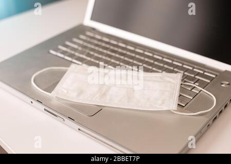 Un masque médical antiviral se trouve sur le clavier d'un ordinateur portable ouvert. Prévention du coronavirus ncov-19. Travailler sur l'ordinateur à domicile pendant la quarantaine. Banque D'Images