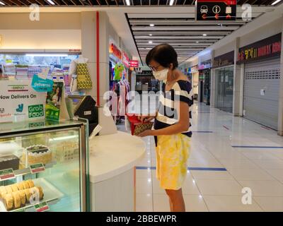 SINGAPOUR – 30 MARS 2020 – une femme singapourienne d'âge moyen portant un masque achète des produits de boulangerie dans le centre commercial Bukit Timah Plaza, à moitié fermé. Reta Banque D'Images