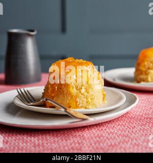 Éponge vapeur individuelle puddings sirop marmelade rouge plateau de table blanc assiettes fourchette gooey collante lambris foncé Banque D'Images