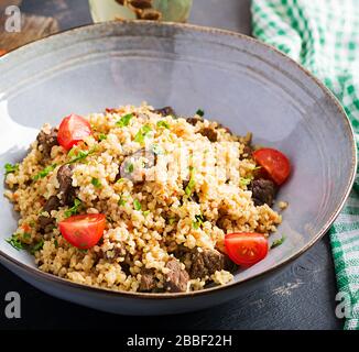 Bubgur pilaf avec viande et légumes. Délicieux déjeuner chaud et sain sur fond noir. Cuisine orientale. Banque D'Images