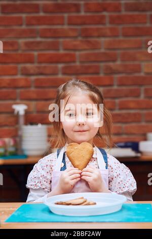 La petite fille se fait un plaisir à partir de cookie cuit fait soi-même. Enfant prenant part à l'atelier de cuisson. Cours de cuisson pour enfants, aspirant petits chefs. Le Banque D'Images