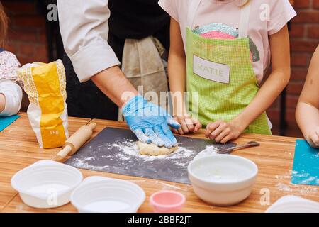 Une fille avec des chefs aide à pétrir la pâte pour cuire le gâteau. Enfant prenant part à l'atelier de cuisson. Cours de cuisson pour enfants, aspirant petits chefs. Banque D'Images