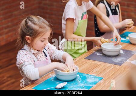 Les petites filles pétrissent la pâte pour faire cuire le gâteau. Les enfants participent à l'atelier de cuisson. Cours de cuisson pour enfants, aspirant petits chefs. Learnin Banque D'Images