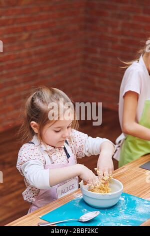 Les petites filles pétrissent la pâte pour faire cuire le gâteau. Les enfants participent à l'atelier de cuisson. Cours de cuisson pour enfants, aspirant petits chefs. Learnin Banque D'Images