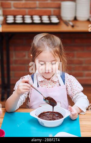 Petit chef remuant le chocolat chaud fondu avec du cacao. Enfant prenant part à l'atelier de cuisson. Cours de cuisson pour enfants, aspirant petits chefs. Learnin Banque D'Images