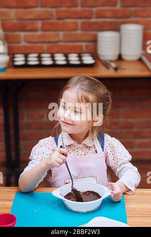 Petit chef remuant le chocolat chaud fondu avec du cacao. Enfant prenant part à l'atelier de cuisson. Cours de cuisson pour enfants, aspirant petits chefs. Learnin Banque D'Images