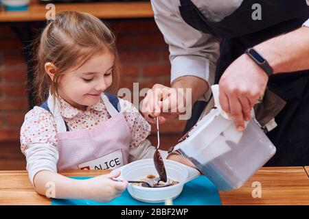 Le chef ajoute du chocolat chaud fondu au cacao dans le récipient. Enfant prenant part à l'atelier de cuisson. Cours de cuisson pour enfants, aspirant petits chefs. Lea Banque D'Images