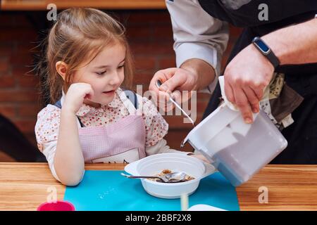 Le chef ajoute du chocolat chaud fondu au cacao dans le récipient. Enfant prenant part à l'atelier de cuisson. Cours de cuisson pour enfants, aspirant petits chefs. Lea Banque D'Images