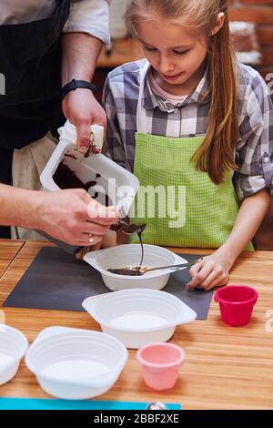 Le chef ajoute du chocolat chaud fondu au cacao dans le récipient. Enfant prenant part à l'atelier de cuisson. Cours de cuisson pour enfants, aspirant petits chefs. Lea Banque D'Images