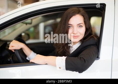 Gai riant la jeune femme assise dans une nouvelle voiture dans une concession de voiture Banque D'Images