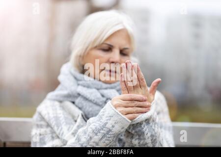 Femme senior avec arthrite frottant les mains Banque D'Images