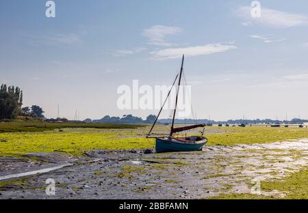 Petit bateau à voile en bois avec voiles à fourrure mis à la terre dans le port de Chichester sur des appartements de boue à marée basse à Bosham, un petit village de la côte sud de l'Angleterre Banque D'Images